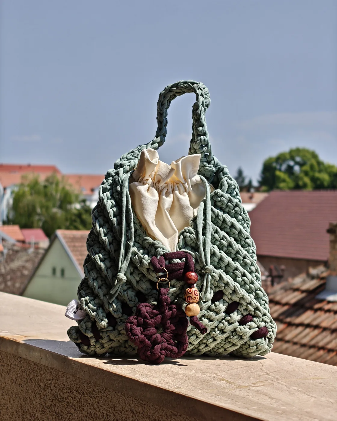Soft Sage crochet bag from the Tria collection, on a terrace ledge