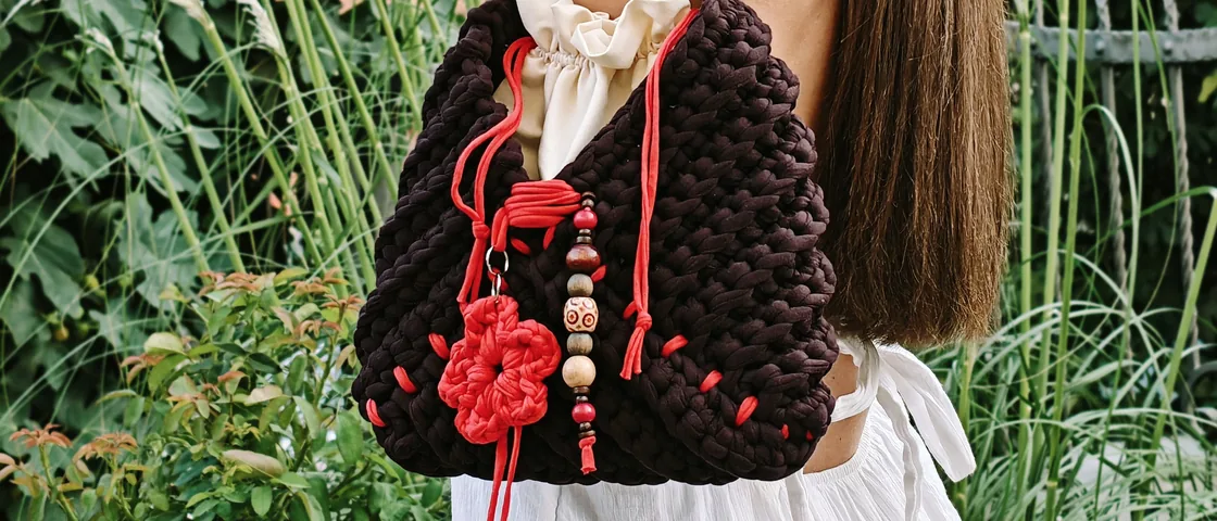 Woman seen from behind carrying the Plum crochet bag, in a garden with pampas grass