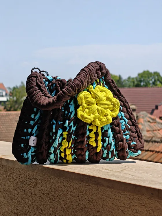 Dark brown crochet bag with turquoise and yellow accents, a crocheted flower and silver rings