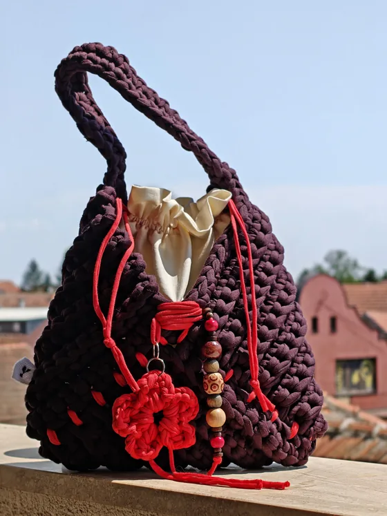 Deep burgundy plum crochet bag with bright red drawstrings and a crocheted flower